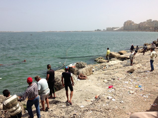 As the men onshore draw the net together, one swimmer hauls the smaller net towards the big looped net.