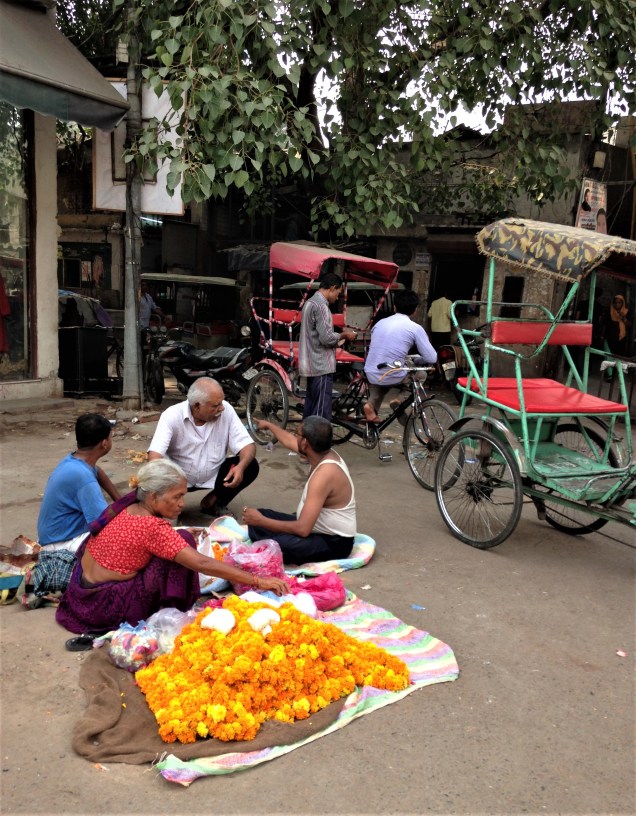 A lady with a heap of marigolds, with several men and two traditional cycle rickshaws behind. Pahar Ganj, Delhi.