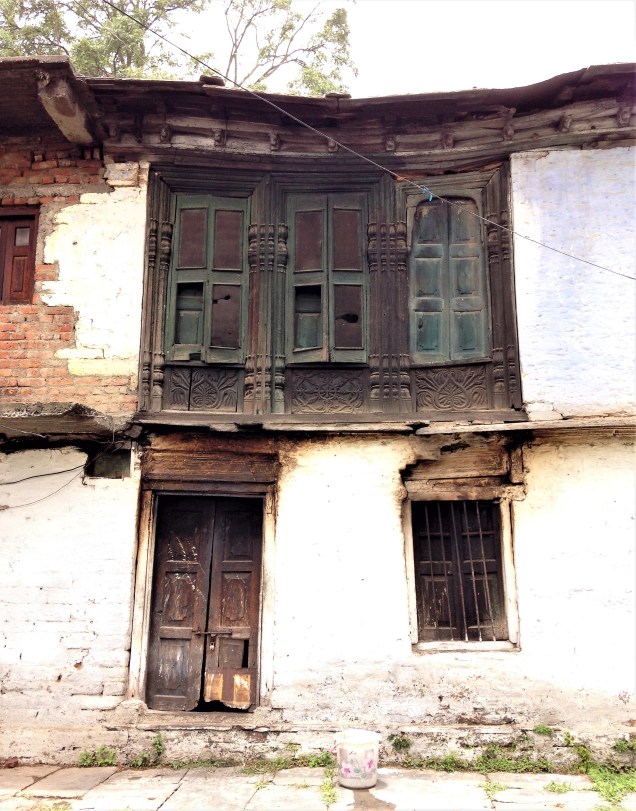 An old brick and stucco house in Almora, with traditional decorated wooden windows. Uttarakhand