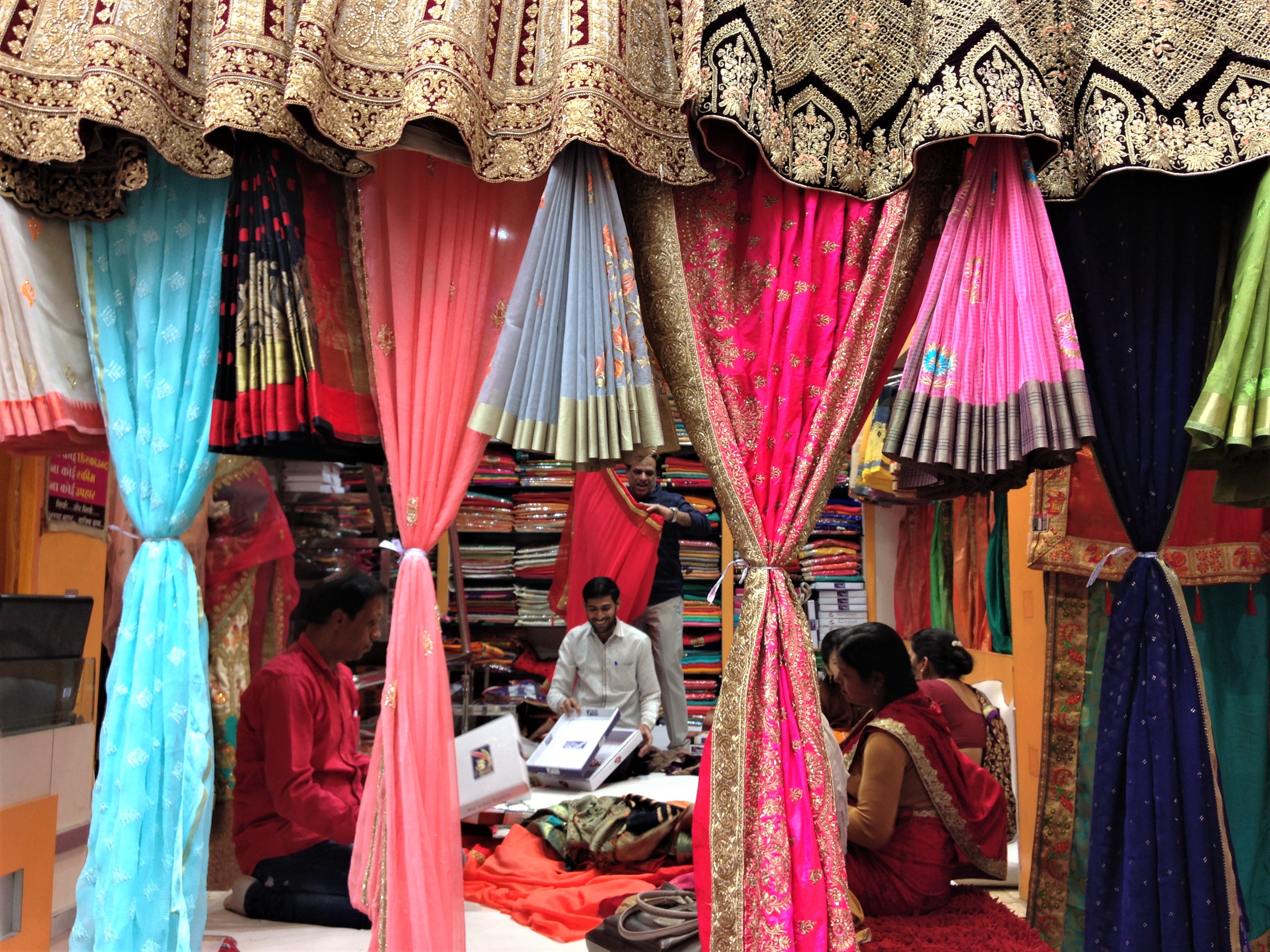 Looking through a curtain of colorful saris into a sari shop, with the proprietor showing saris to some ladies. Cloth market district, Indore, Madhya Pradesh.
