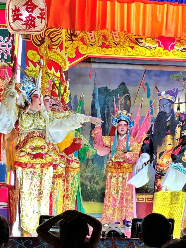 Chinese opera actor gesturing to other actors across the stage